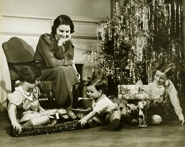 Mother watching three children playing by Christmas tree, (B&W)