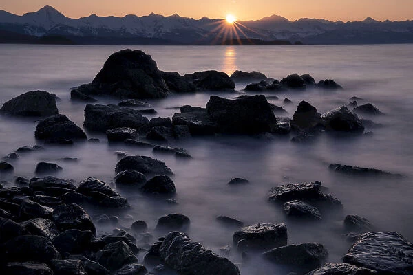 Silhouette of rock formations and misty water with sun setting behind mountains, USA