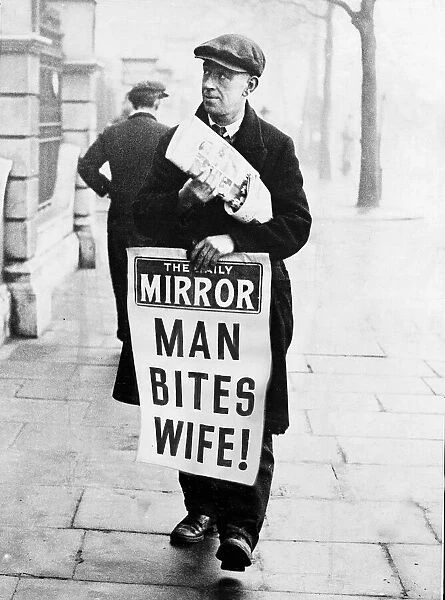 Daily Mirror newspaper vendor carrying advertising hoarding with Man Bites Wife headline