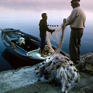 Two fishermen sort their nets on stone quayside - Fetheye