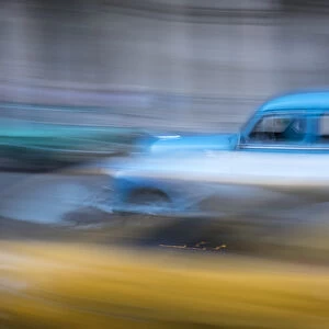 Cuba, Havana. Classic cars speed by in a blur along the streets of the city