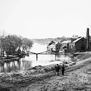 CIVIL WAR: FALL OF RICHMOND. View of the Tredegar Iron Works, with footbridge to Neilsons Island. Photographed in April 1865 by Alexander Gardner