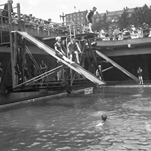 Swimmers enjoying the water chute and diving boards at the open air swimming pool
