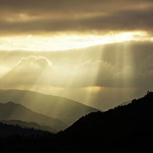 Shafts of light at dusk over Wrynose pass and the Coniston hills from Ambleside, Lake District